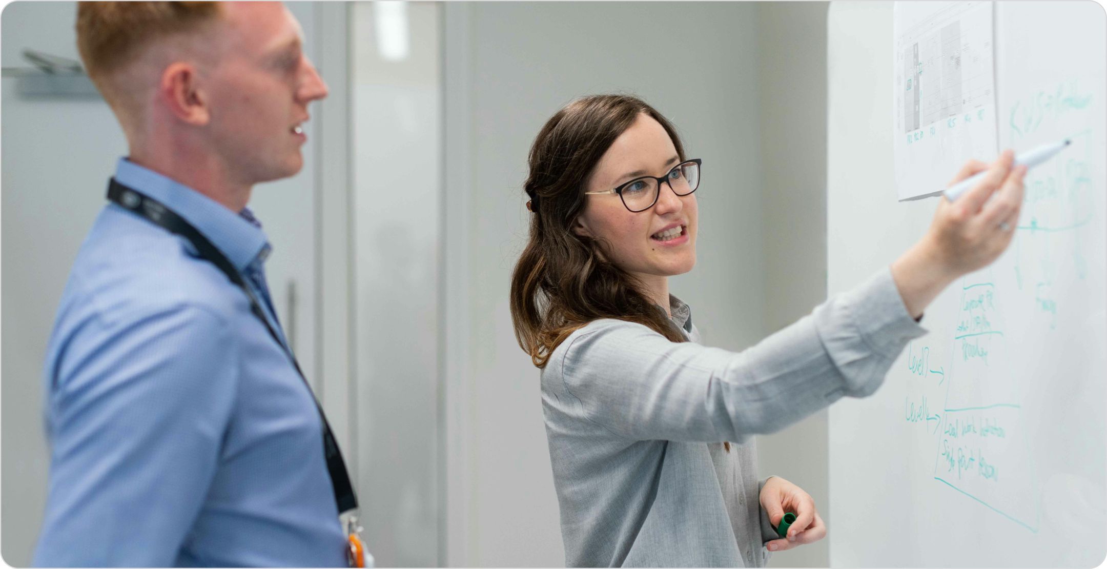 A businesswoman pointing at a whiteboard  with a marker, talking with a colleague; illustrating key drivers analysis