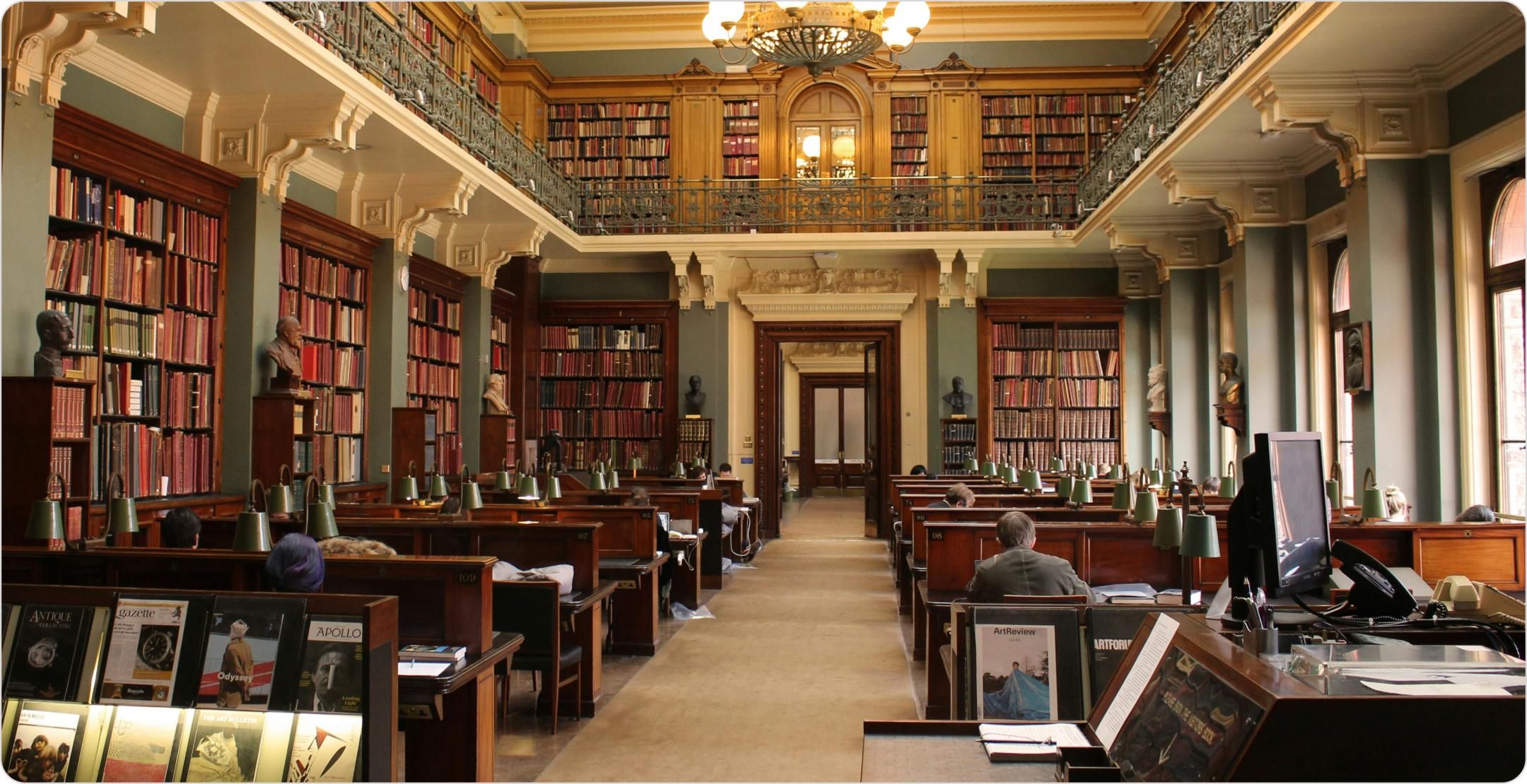 The interior of a two story library with books lining the walls and study cubicles in the center of the room. Represents secondary research.