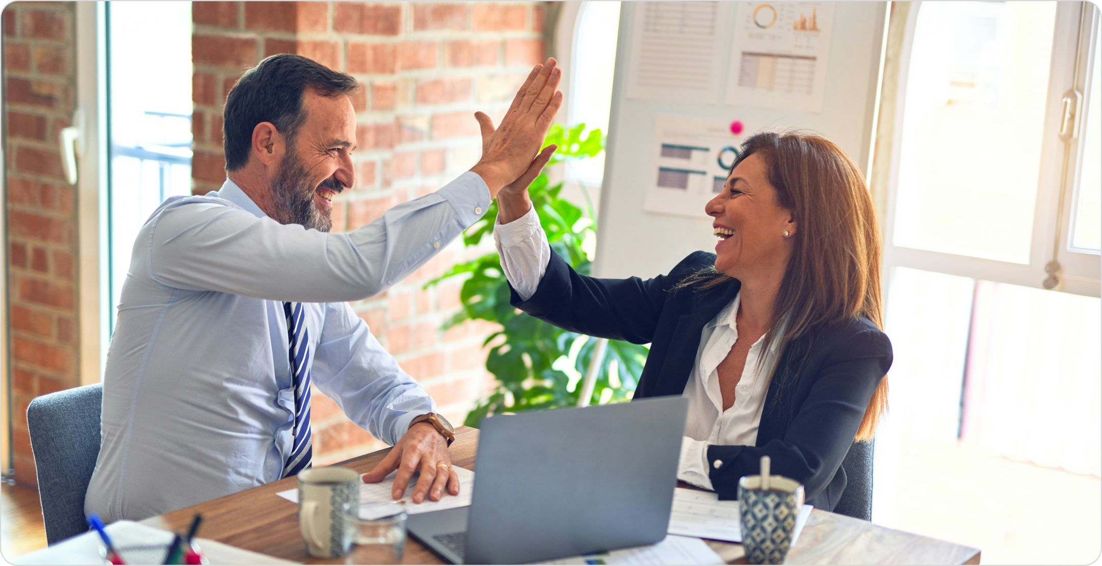 A business man and woman doing a high-five at a workstation. Representing business growth and success with diagnostic analytics