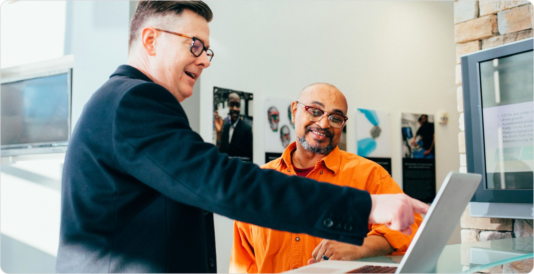 Two businessmen smiling and looking at a laptop: signifying prescriptive analytics examples.