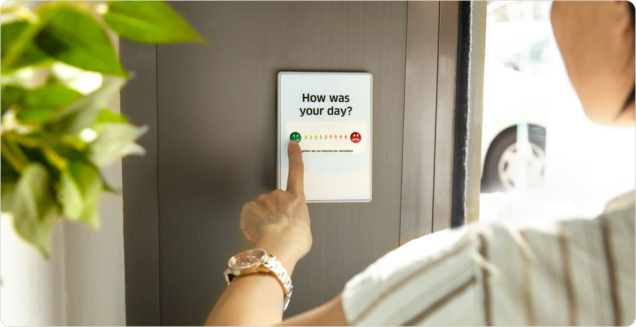 A woman answering a survey question on a tablet mounted on a wall.