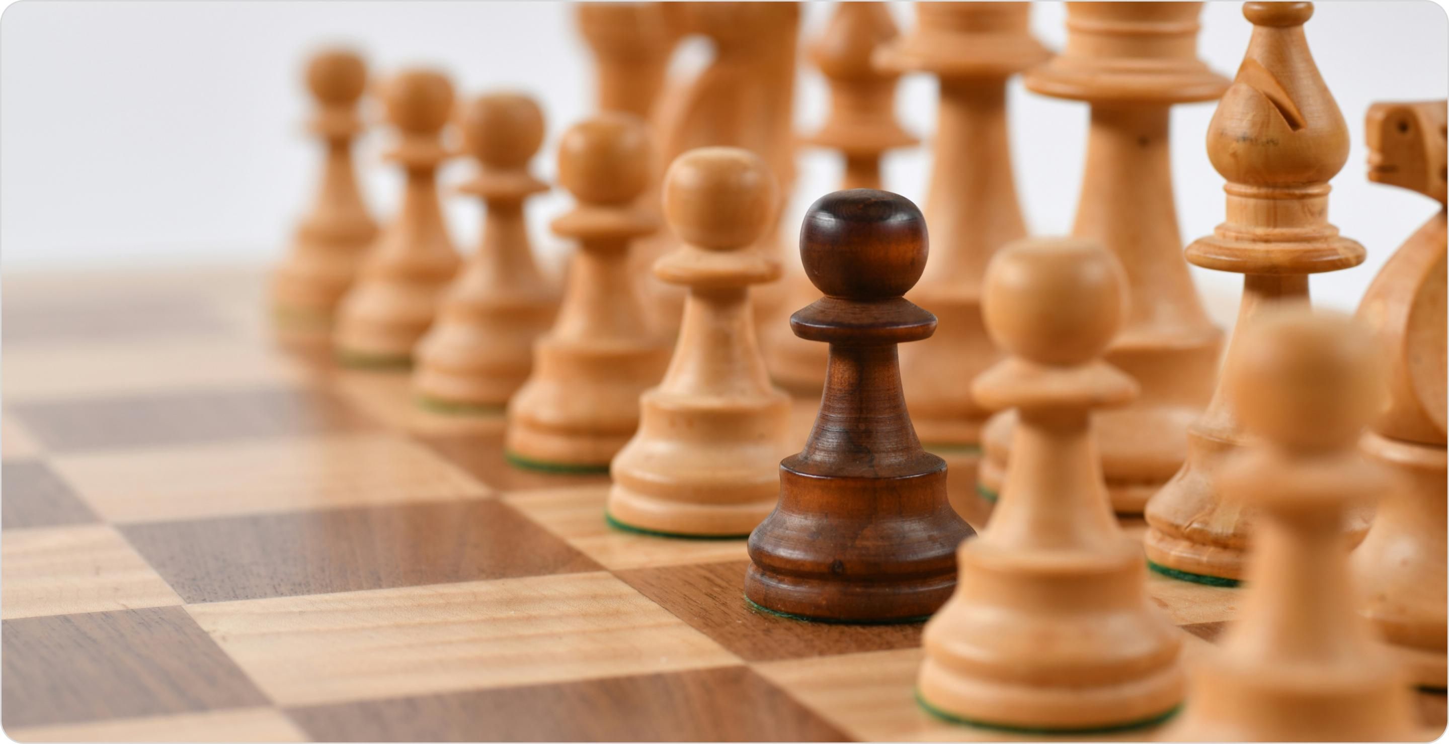 Close up of a chess board set up with pieces in starting positions. One pawn is dark amongst the light colored pieces to illustrate market segment identification.
