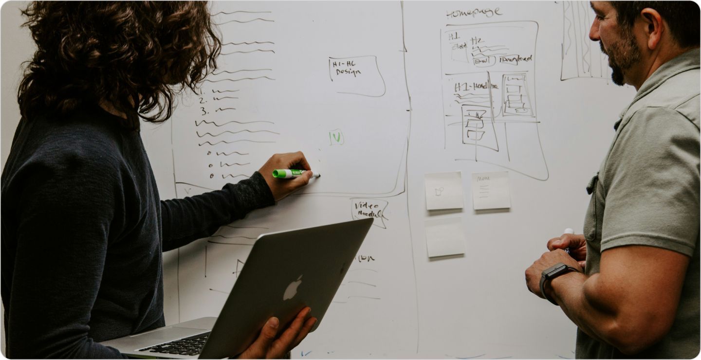 Two colleagues, a woman and a man, planning their survey design on a whiteboard. 